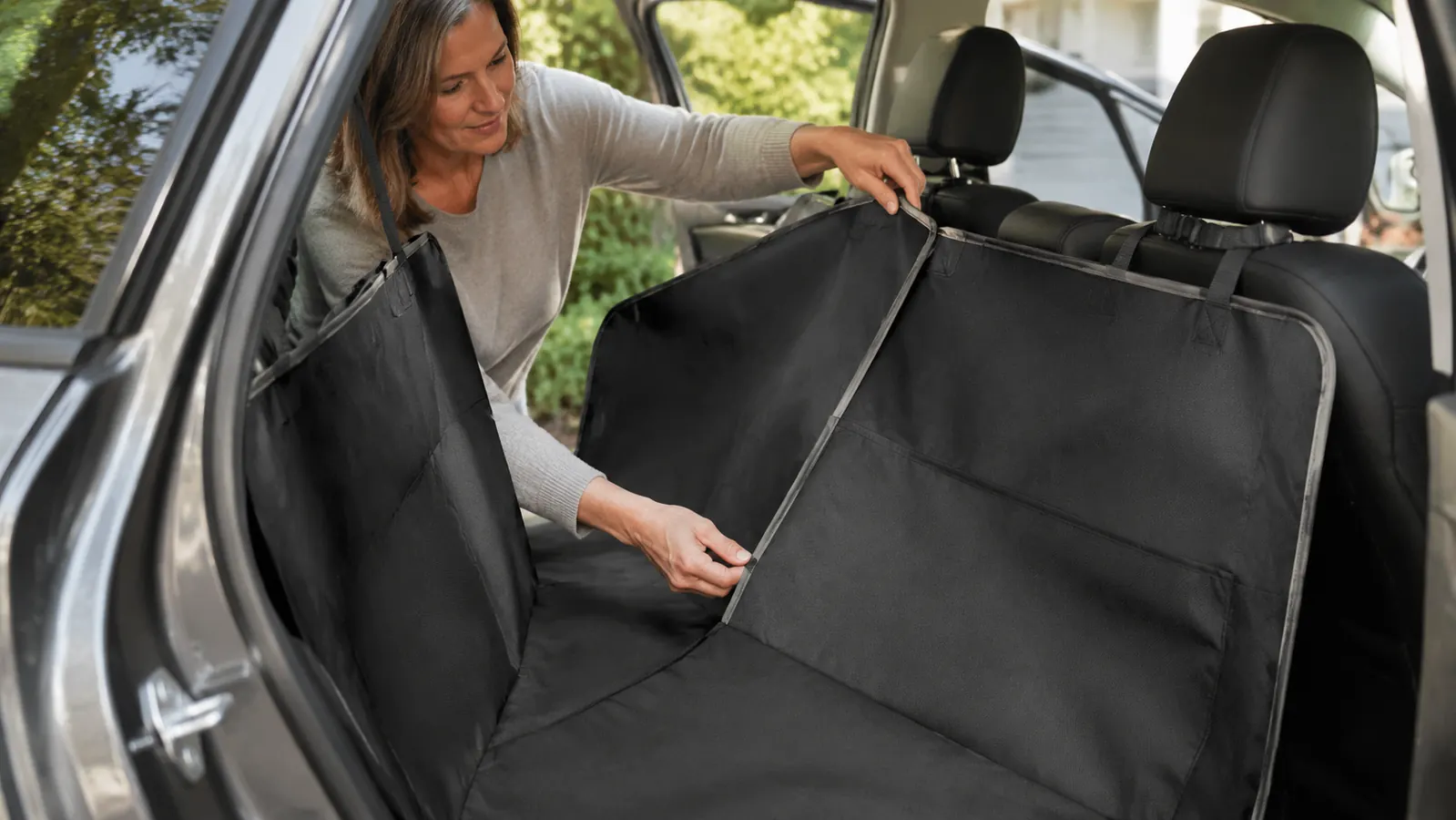 A person's hands adjusting the hammock panel of a dog seat cover over the back seat, one strap held up, casual daylight